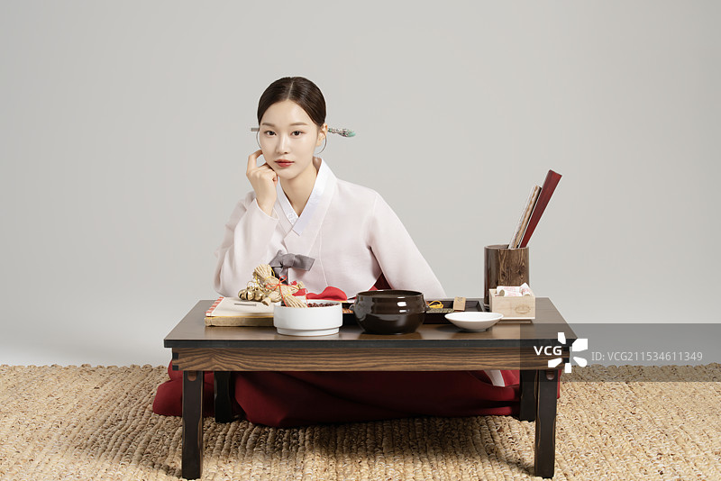 一位年轻的萨满穿着韩服，坐在桌子前，桌上摆放着萨满工具，正在思考。图片素材