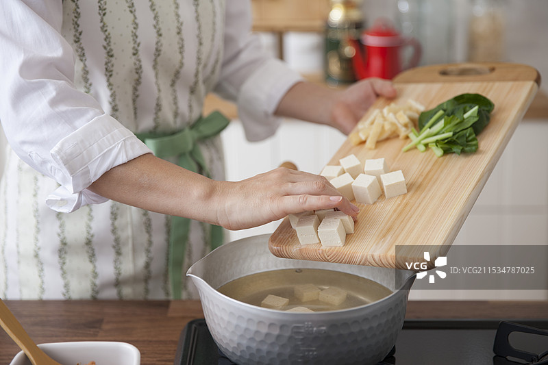女人将味噌汤的配料放入锅中图片素材