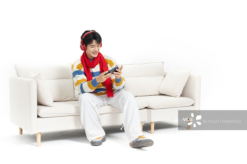 坐在沙发上手拿手机头戴红色耳机的年轻男孩图片素材