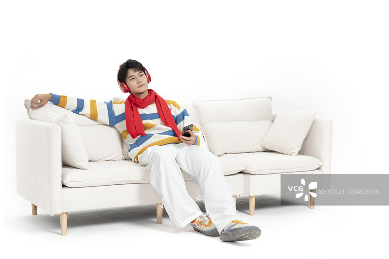 坐在沙发上手拿手机头戴红色耳机的年轻男孩图片素材