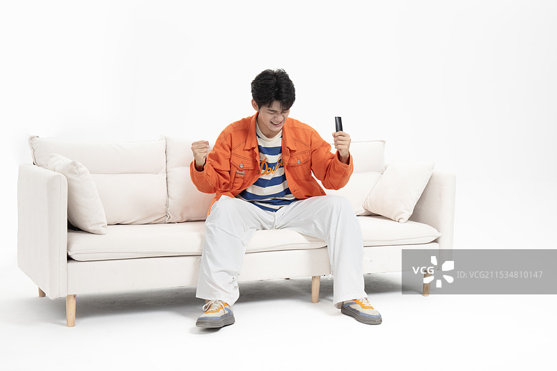 手拿遥控器坐在沙发上的年轻亚洲男人图片素材