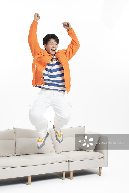 手拿遥控器坐在沙发上的年轻亚洲男人图片素材