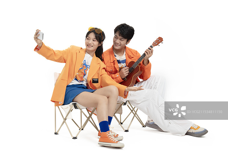 坐在户外椅上手拿手机与尤克里里的年轻情侣图片素材