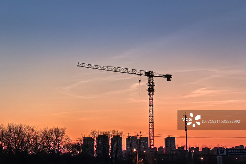金橙色的余晖下，城市边缘的天际线剪影，一座塔吊静静地挺立图片素材