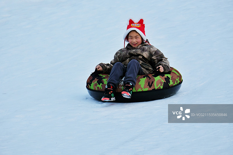 冬天。滑雪场。玩儿滑雪圈的虎头帽少年图片素材