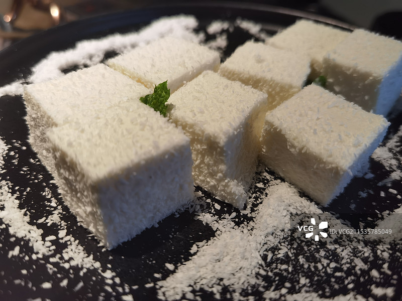 椰蓉洒满黑盘，椰奶方块洁白如雪，简约精致图片素材