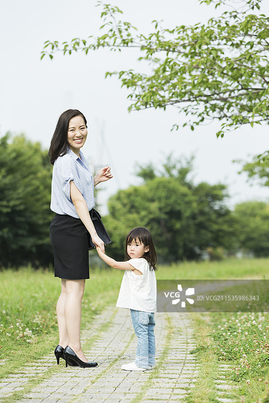父母与孩子手牵手走在郁郁葱葱的绿树之间图片素材