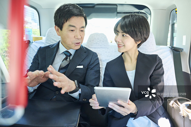 一位50多岁的男性办公室工作人员和一位30多岁的女性办公室工作人员在出租车内开会图片素材