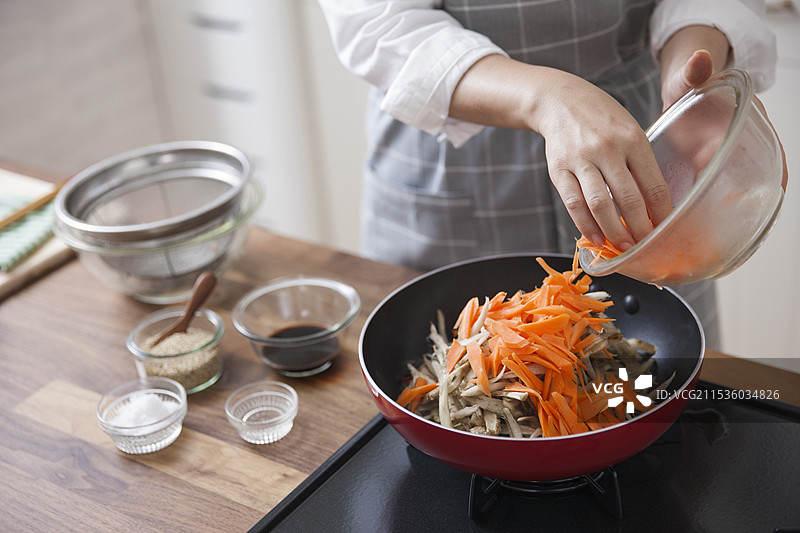 女人在平底锅中煎炒牛蒡和胡萝卜图片素材