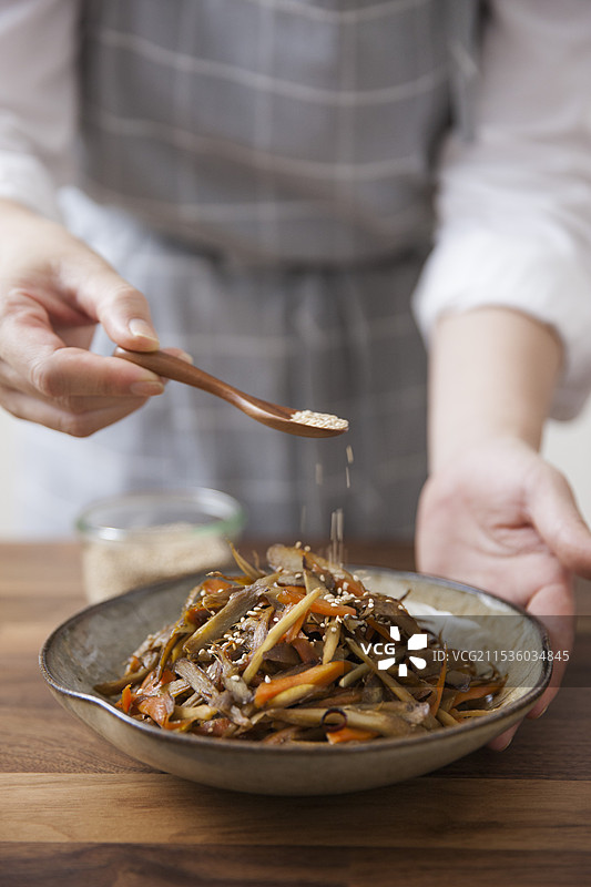 女人在金平牛蒡上撒芝麻图片素材