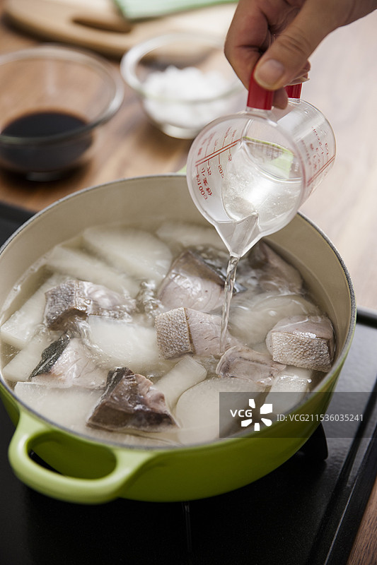 女人将萝卜和黄尾鱼炖煮，并加入清酒图片素材