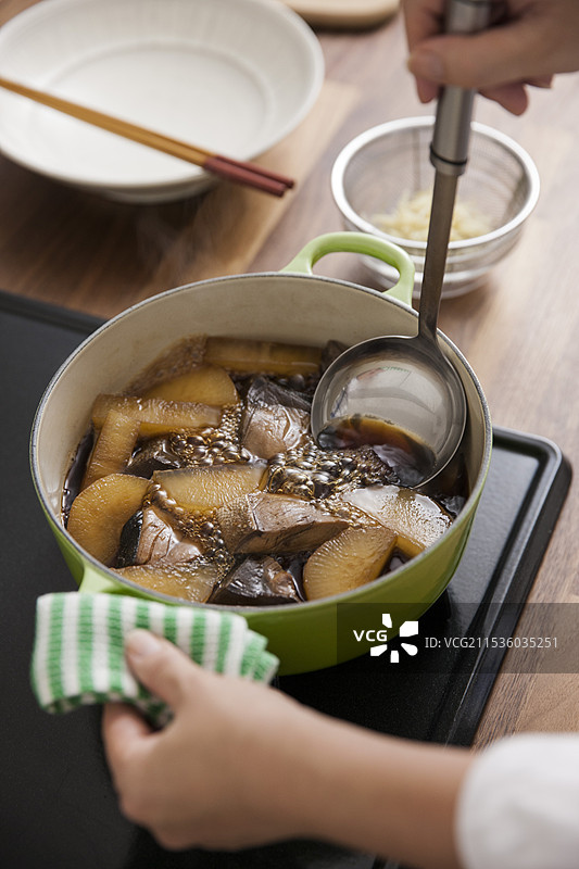 女人将萝卜和黄尾鱼炖煮，并加入酱油。图片素材