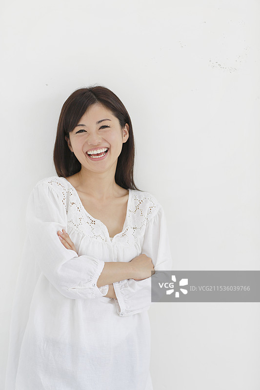 女人在白色墙壁前双臂交叉大笑图片素材