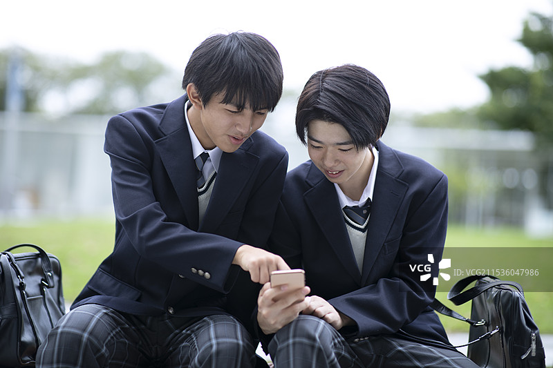 高中男生一边看着智能手机一边交谈图片素材