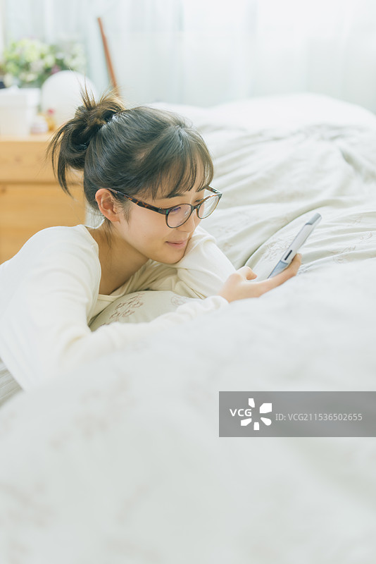 年轻女性在床上看智能手机图片素材