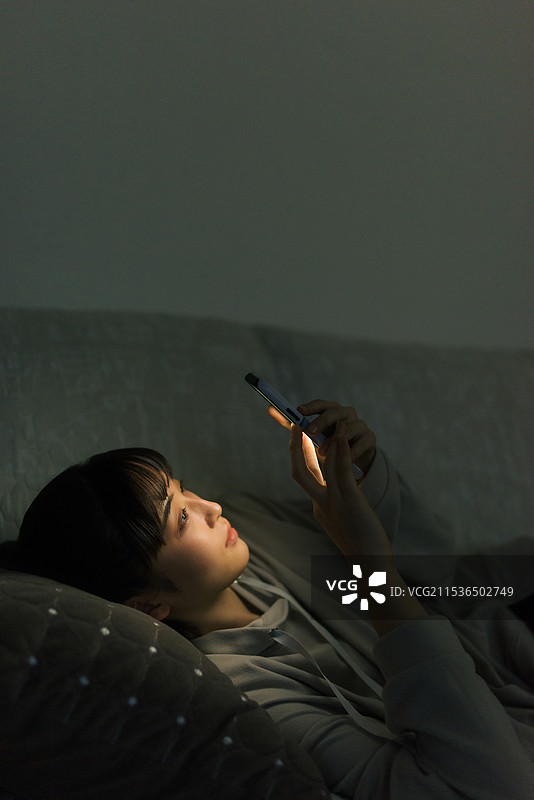 年轻女性在夜晚关灯时看手机图片素材