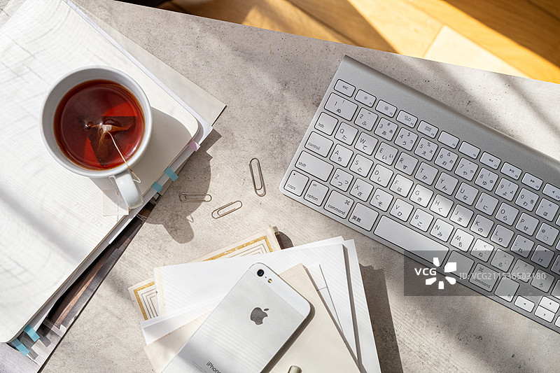 窗边桌子上的键盘、手机、回形针、笔记本和文件图片素材