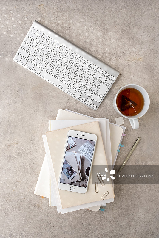 灰色桌子上的键盘、茶、手机、笔记本、钢笔和夹子图片素材