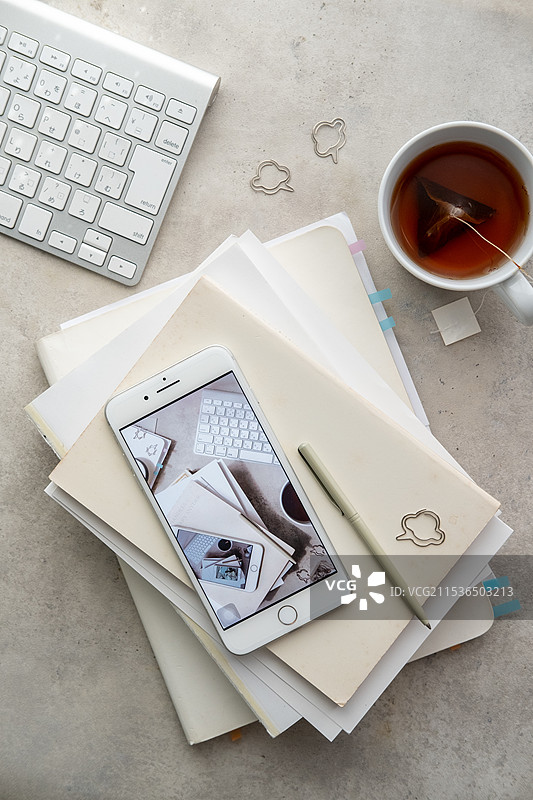 灰色桌子上的键盘、茶、手机、笔记本、钢笔和夹子图片素材