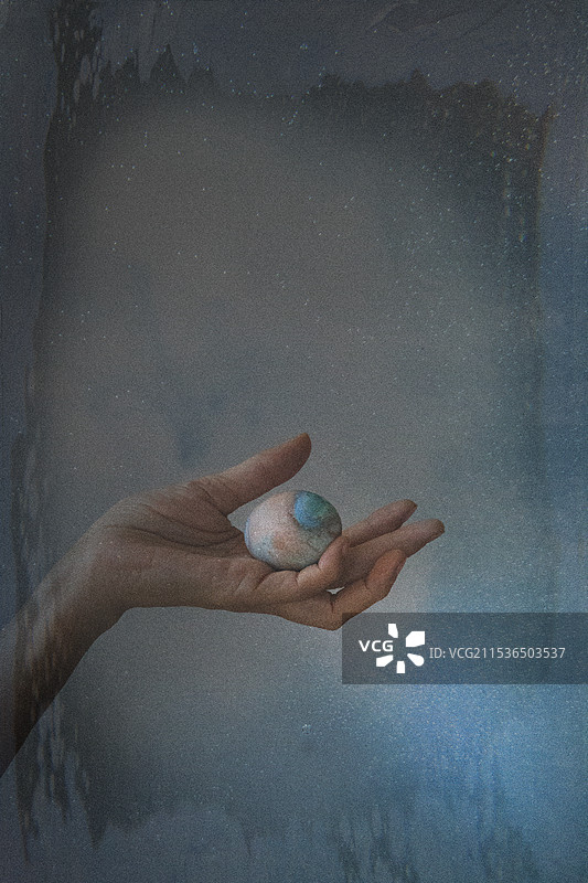 一张合成照片，展示一位女性的手握着一个太空蛋和一个人造星空。图片素材