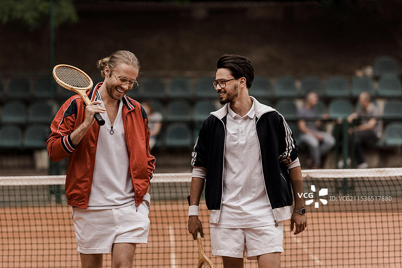 微笑的复古风格网球运动员在网球场上手持球拍走动图片素材