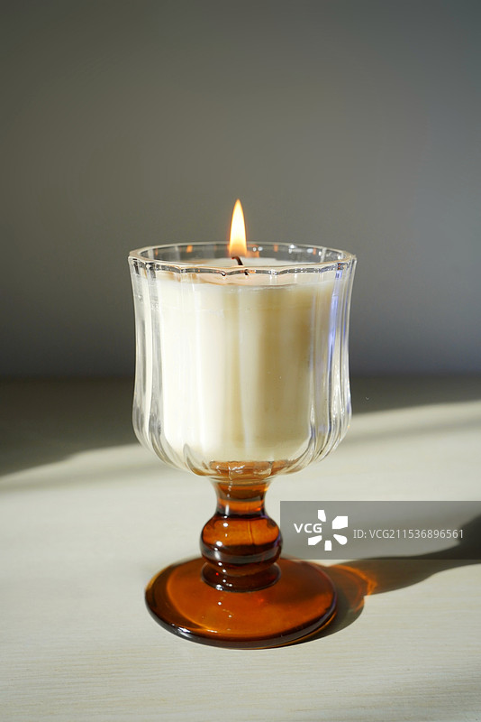 白色桌面上茶色玻璃酒杯和燃烧的香薰蜡烛特写图片素材