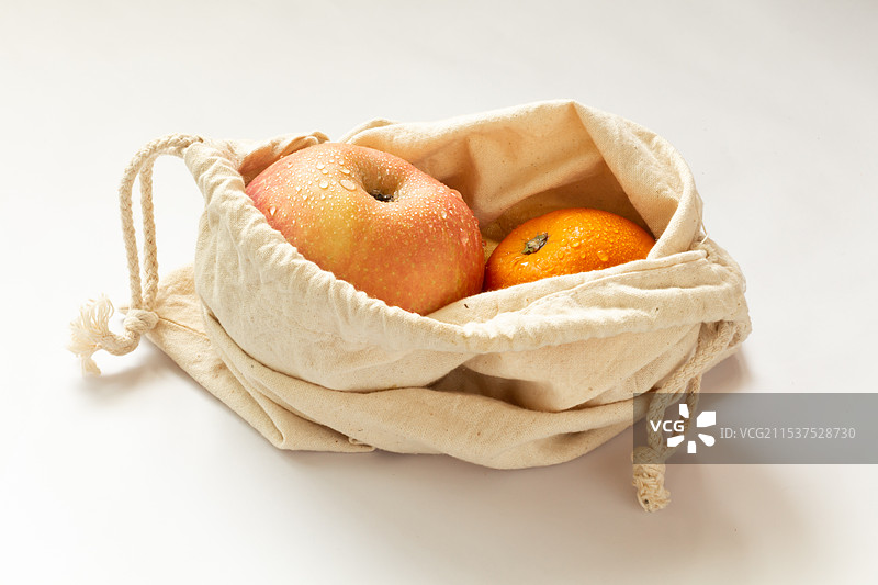 白色背景上白色环保帆布袋中的水果苹果和橘子图片素材