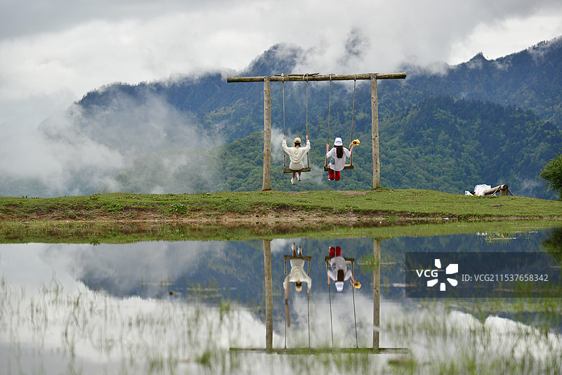 天地云海间，女孩们坐在高原湖边的秋千上摇荡图片素材