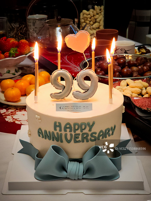 一个淡黄色的生日蛋糕，点燃了蜡烛，桌上摆满了鲜艳的水果，一份浓浓的纪念庆典氛围图片素材