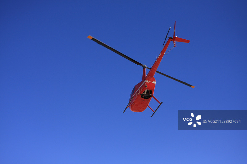 红色直升机在蓝天下飞行的低角度视图图片素材