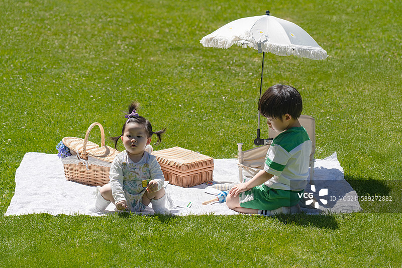遮阳伞下穿运动短袖装男孩与女婴妹妹在公园草坪上玩耍图片素材