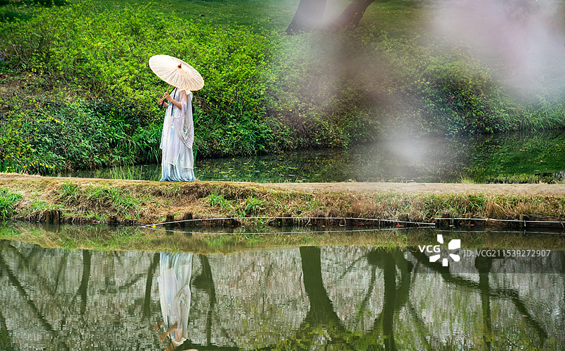 烟雨迷蒙的江南春天，无锡鼋头渚的樱花盛开密密麻麻挂满枝头，一个穿着汉服的女孩撑着油纸伞倒影在平静水面图片素材