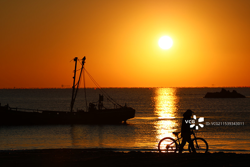 清晨橙色天空下海边人物与自行车剪影-3图片素材