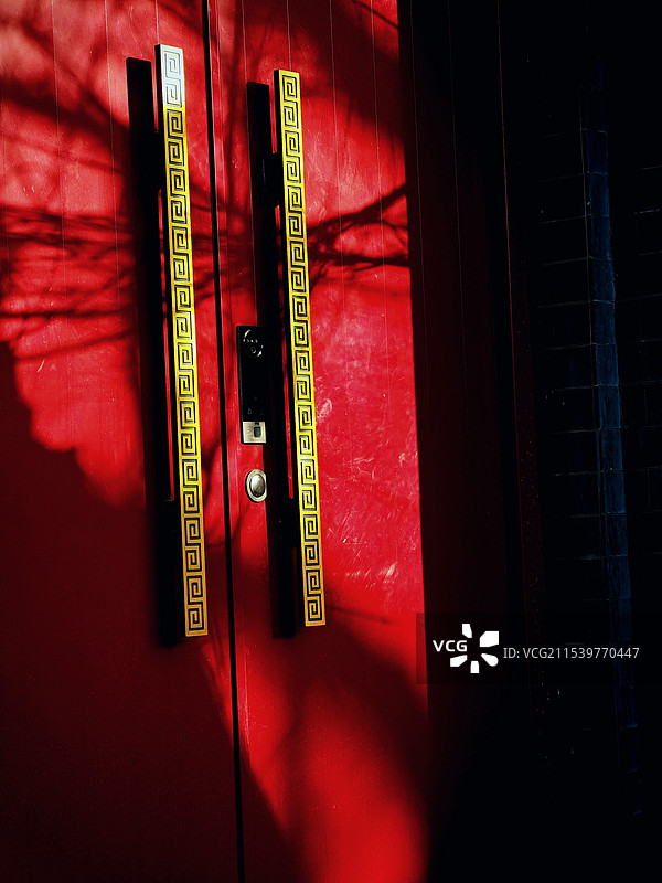 红门靓影：阳光打在一处红门上，把树枝的影子印在了上边，黄色的门拉手与红色门形成了色彩对比，虚实对比。图片素材