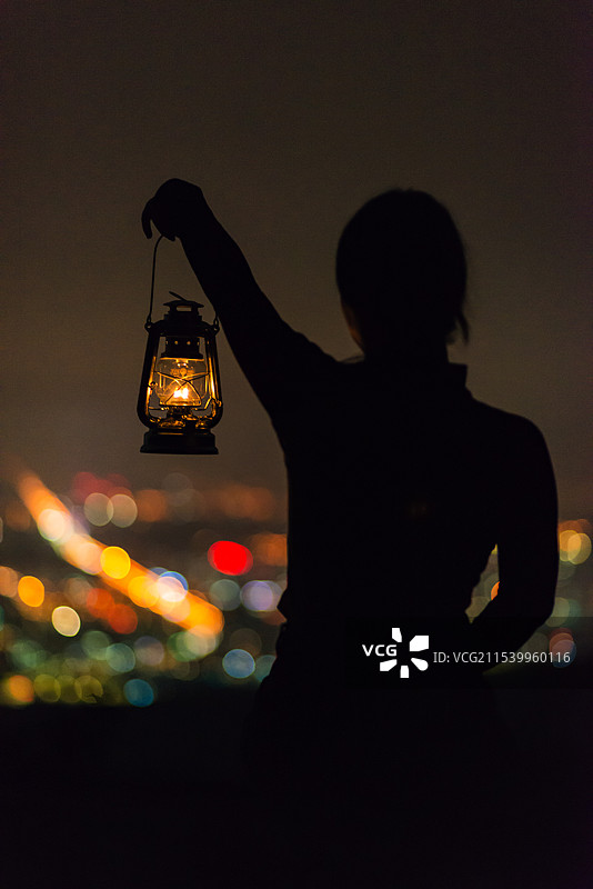 夜晚在城市高处拿着煤油灯的人像剪影图片素材