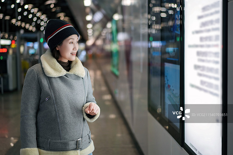 地铁站穿着冬装的女人与数字显示器互动图片素材