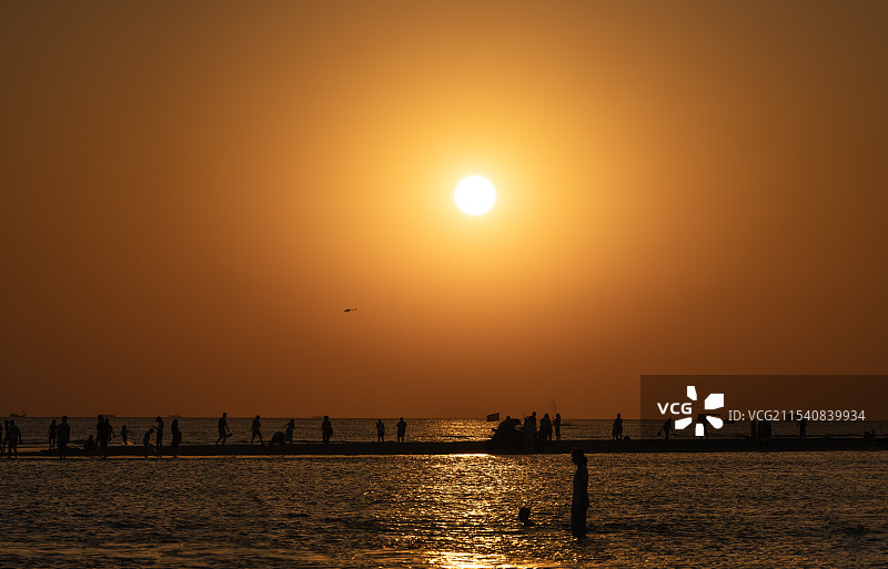 日落时分，橙色天空下，正在海滩上享受的人们的唯美画面图片素材