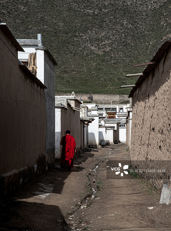 拉卜楞寺一个红袍僧人步行在藏式民居建筑的阴影下图片素材