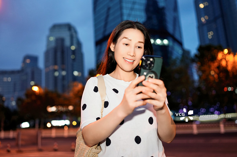 年轻女子在繁忙的城市夜晚与智能手机互动i图片素材