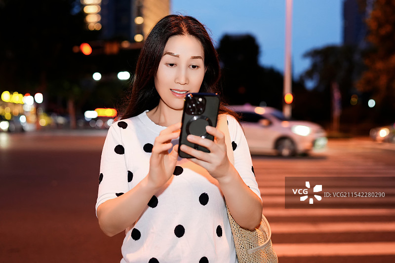 年轻女子在繁忙的城市夜晚与智能手机互动i图片素材