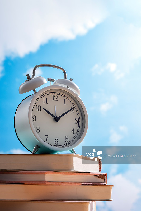 在晴朗的蓝天下在一摞书上的闹钟图片素材