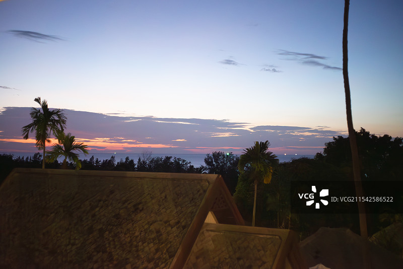 清晨时分，天空呈现出蓝紫色渐变，远处有粉色云霞，近处可见棕榈树和茅草屋顶，仿佛是一处热带地区的美丽景图片素材