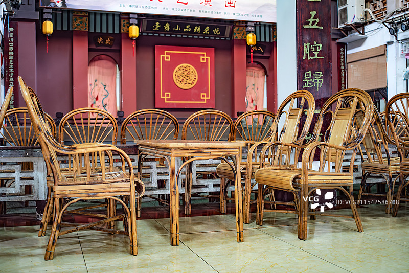 套中式风格的竹制桌椅，摆放在一个具有传统建筑元素的室内环境中，背景墙上有红色装饰和书法字样，充满古典图片素材
