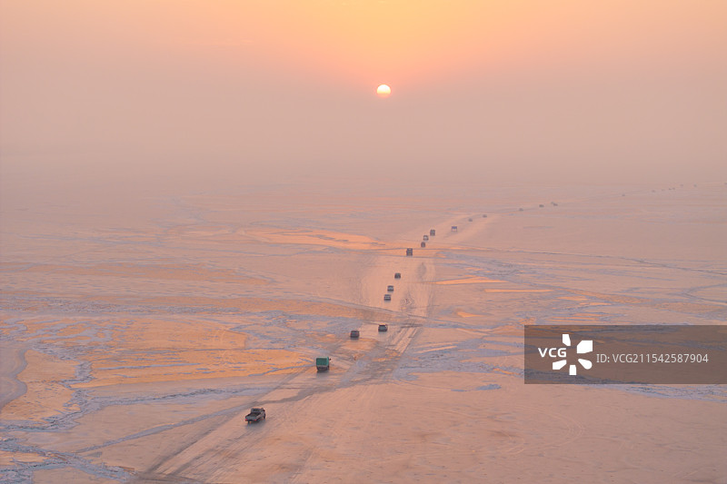 航拍冬季日出时行驶在冰封的吉林松原查干湖上的汽车车队图片素材