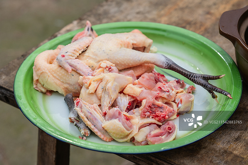 一个绿色盘子里放着一只被拆解的鸡，鸡肉和鸡骨清晰可见，盘子置于木质桌面上。图片素材