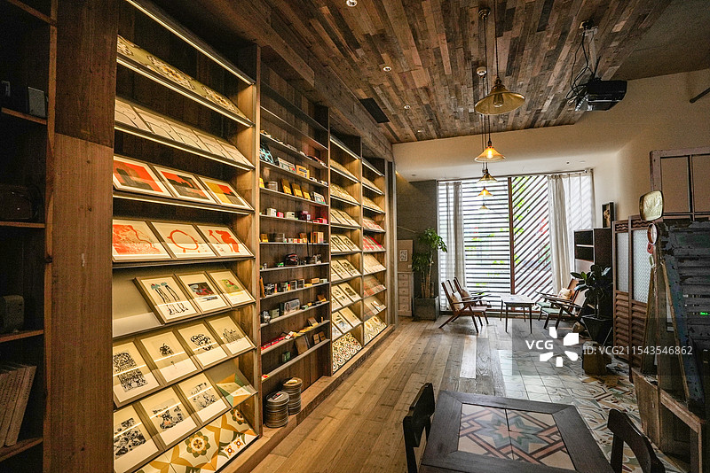 室内空间，木质天花板与地板，左侧书架摆满物品，右侧桌椅靠窗，绿植点缀，光线明亮，氛围温馨舒适。图片素材