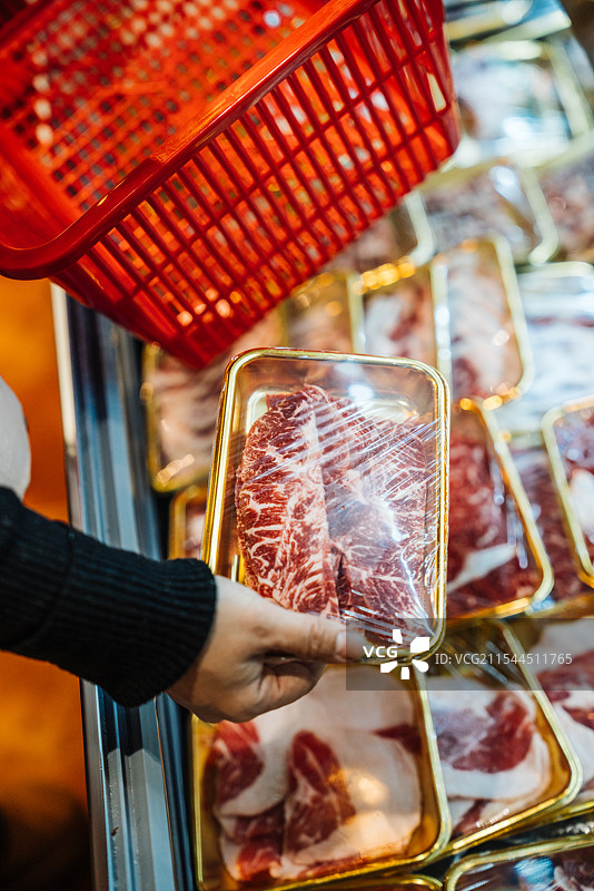 一个人在超市冷柜里挑选新鲜肉类和食材图片素材