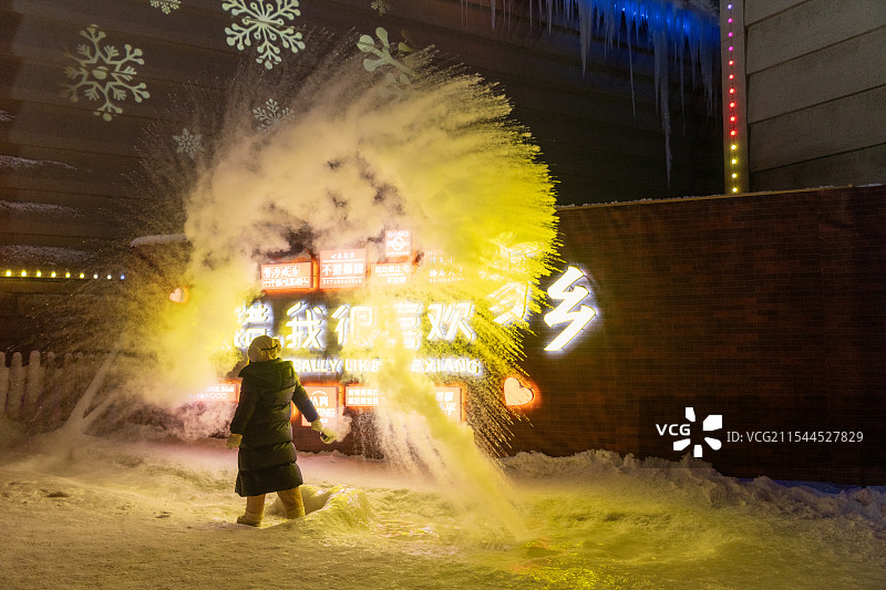 东北雪乡冬季特色娱乐项目，一个人在寒冷的灯光下泼水成冰图片素材