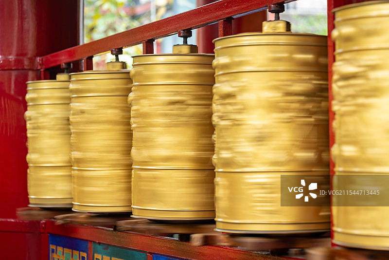 金色圆柱整齐排列在红色背景前，表面光滑反射光泽，绿色植物增添自然色彩，彰显庄重神秘之感。图片素材