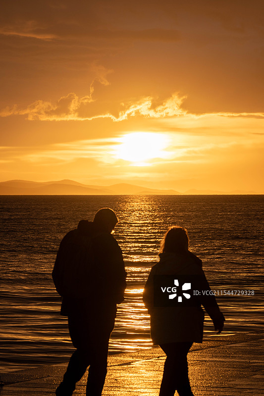 落日余晖走在海边的一对情侣/朋友/夫妻的剪影图片素材